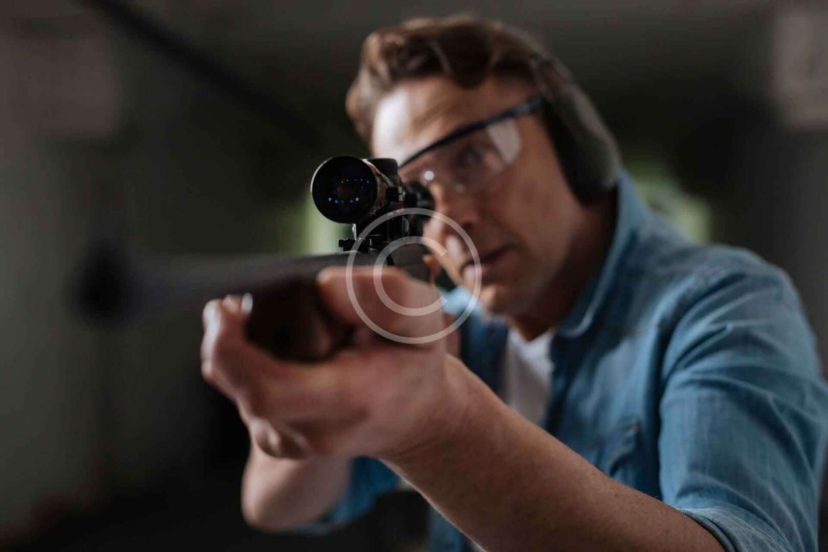 A man aiming at a rifle in a shooting range.