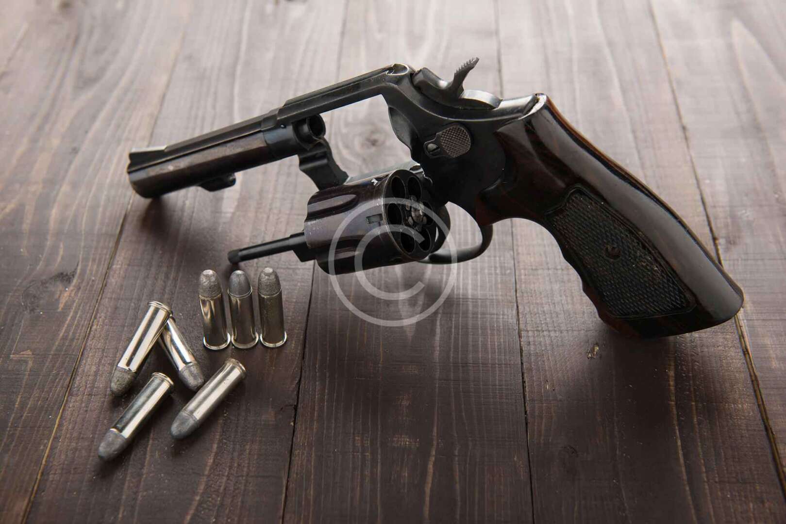 A revolver and bullets on a wooden table.