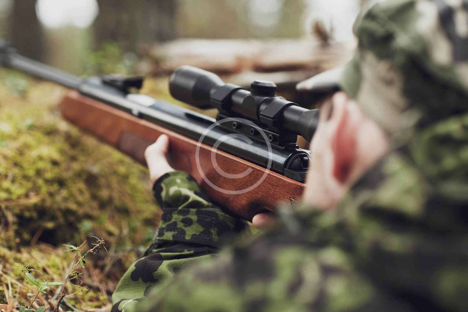 A man in camouflage shooting a rifle in the woods.